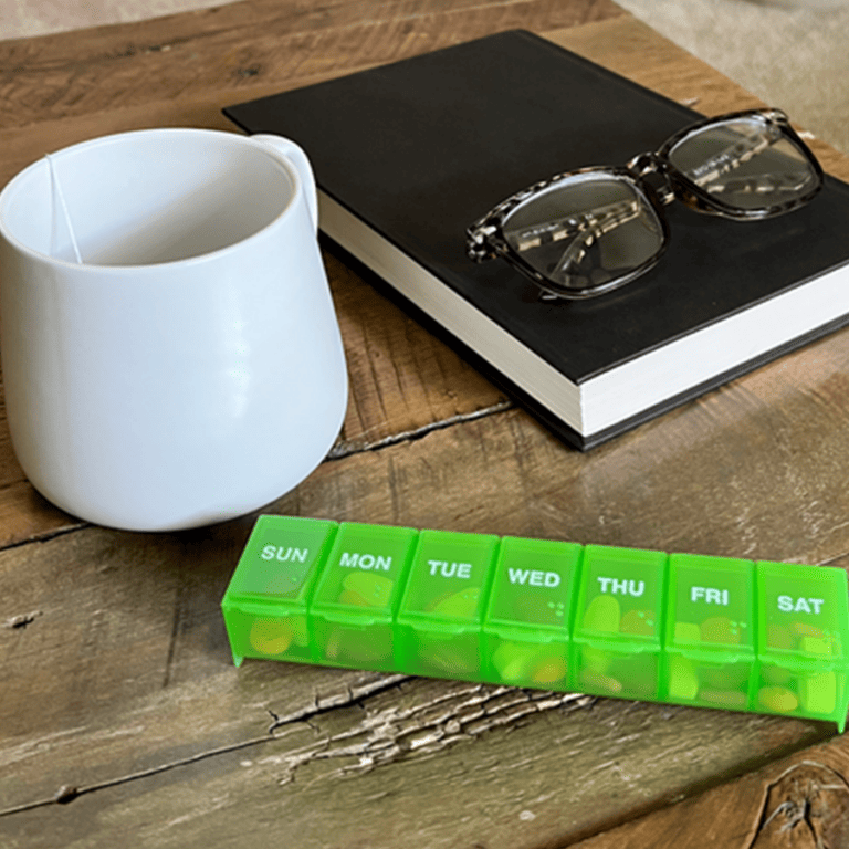 Pill container near coffee cup, reading glasses, and book